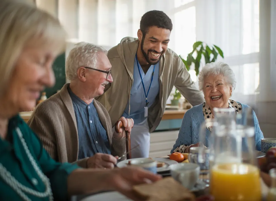 A care worker sharing breakfast with older adults at a kitchen table