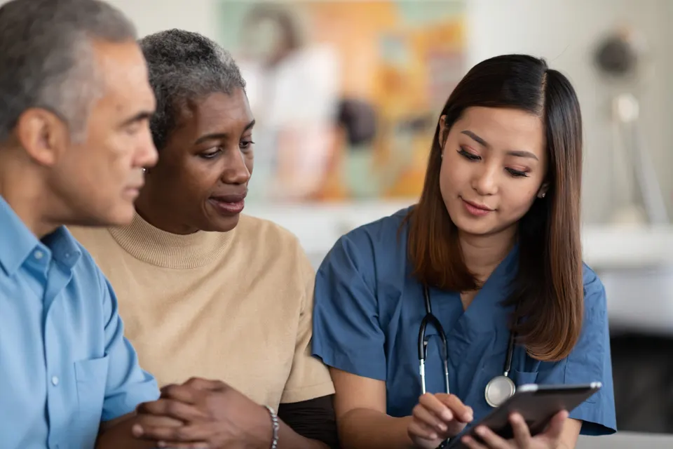 A nurse reviewing information on a tablet with two family members